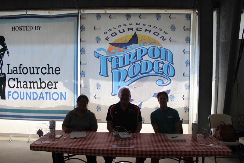 Three people sitting at a table in front of a tarpon rodeo sign