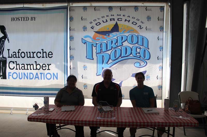 Three people sit at a table in front of a tarpon rodeo sign