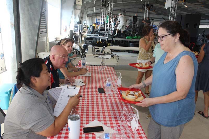 A woman is serving food to a group of people at a picnic table.