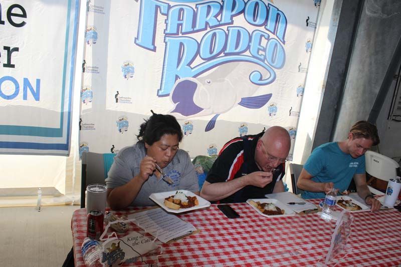 A group of people sitting at a table eating food in front of a sign that says tarpon rodeo