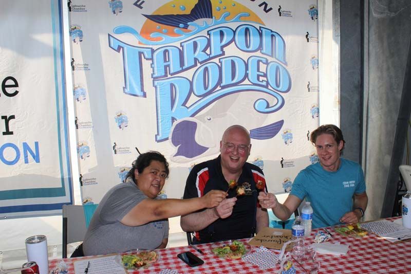 Three people are sitting at a table in front of a tarpon rodeo sign