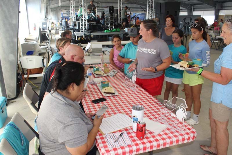 A group of people are standing around a table with a checkered tablecloth.