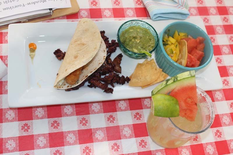 A plate of food on a checkered table cloth next to a glass of watermelon juice