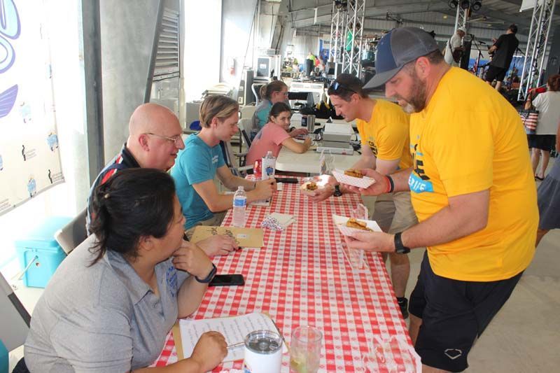 A man in a yellow shirt is serving food to a group of people sitting at a table.
