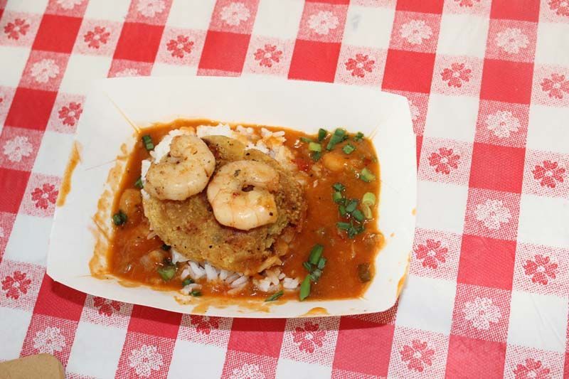 A paper plate of food with shrimp and rice on a checkered table cloth.