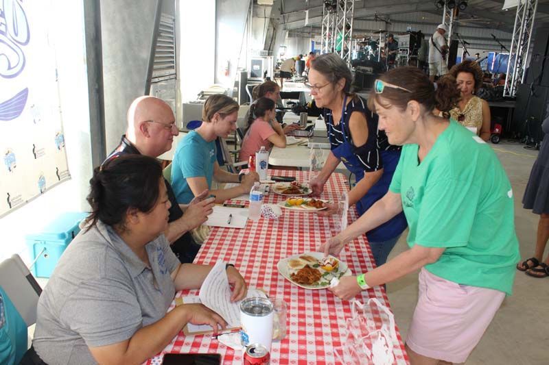 A woman in a green shirt is serving food to a group of people at a table.