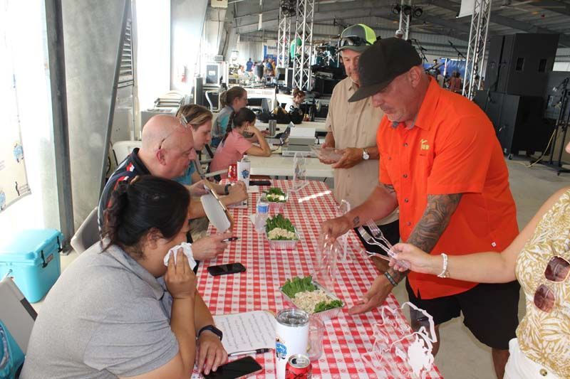 A man in an orange shirt is serving food to a group of people at a table.