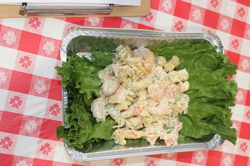 A foil container filled with shrimp salad and lettuce on a checkered table cloth.