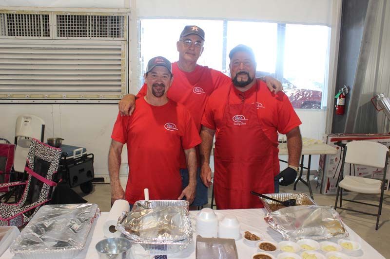 Three men in red shirts are posing for a picture in front of a table.