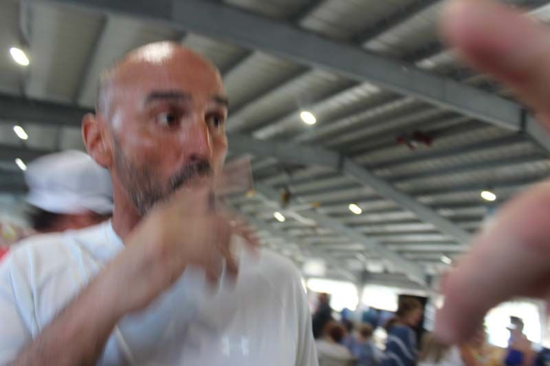 A man with a beard is covering his mouth with his hand in a crowded room.