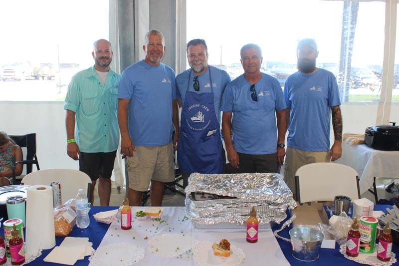 A group of men are standing around a table with food on it.