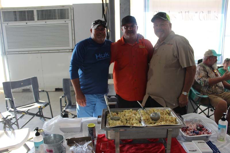 Three men are posing for a picture in front of a buffet table.