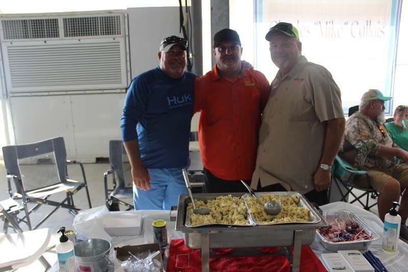 Three men are posing for a picture in front of a buffet table.