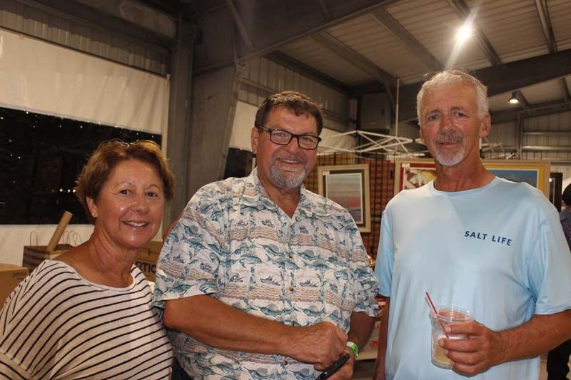 Three people are standing next to each other in a room . one of the men is wearing a salt life shirt.