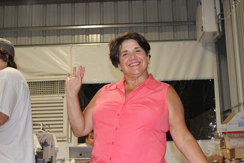 A woman in a pink shirt is smiling and waving at the camera.