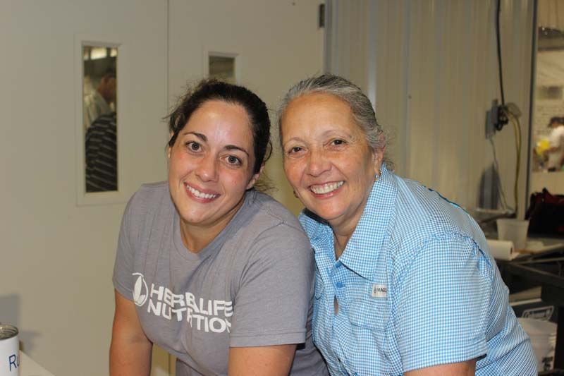 Two women are posing for a picture and one is wearing a herbalife shirt.