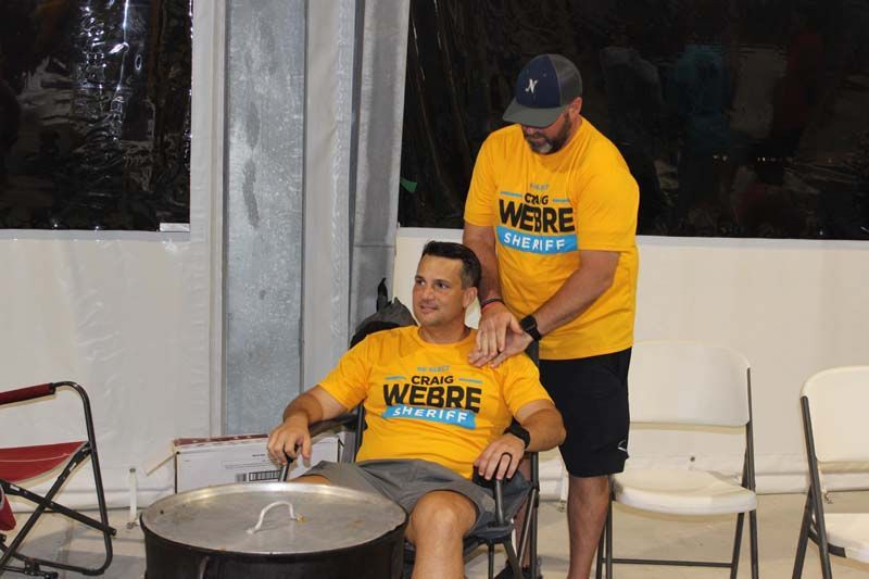 A man in a wheelchair is being helped by another man in a yellow shirt.