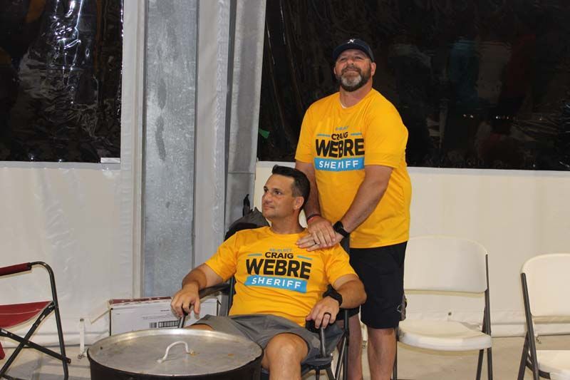Two men wearing yellow shirts that say we are standing next to a man in a wheelchair