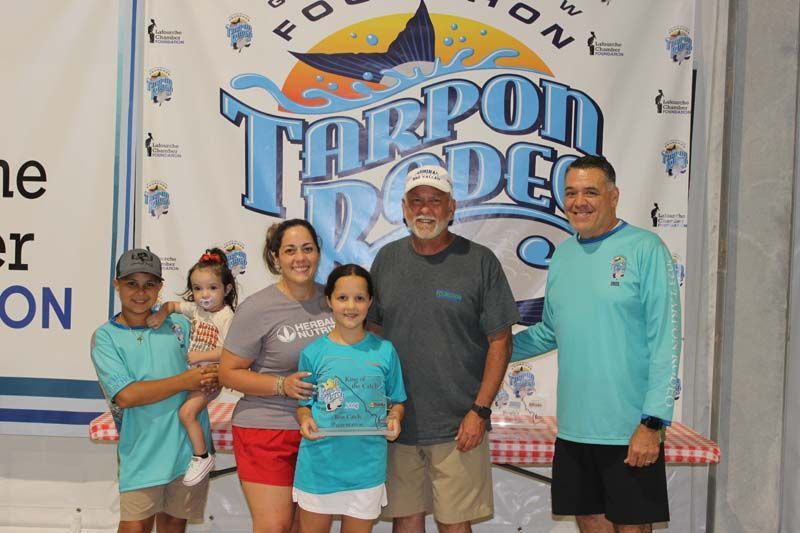 A group of people standing in front of a tarpon rodeo banner.