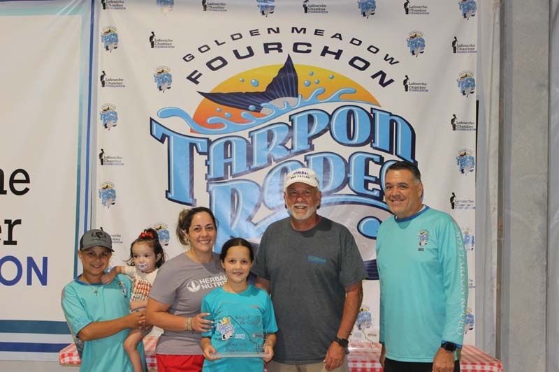 A group of people standing in front of a tarpon rodeo banner