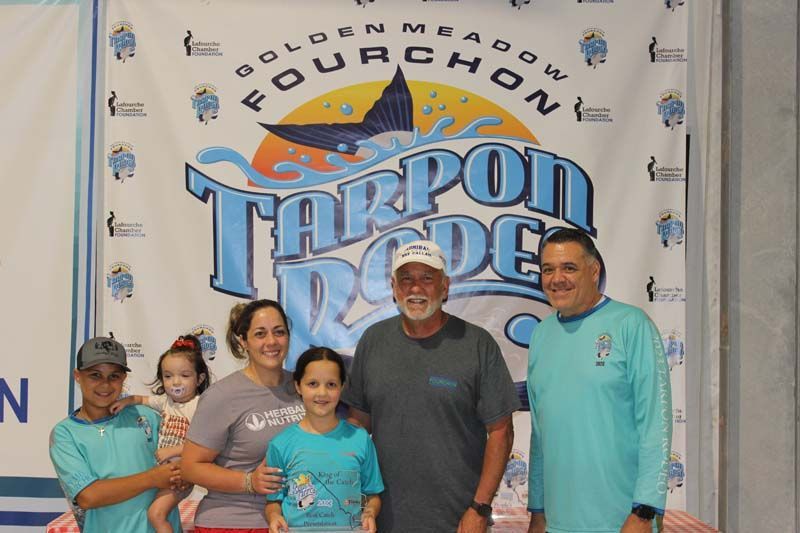 A group of people standing in front of a tarpon rodeo banner