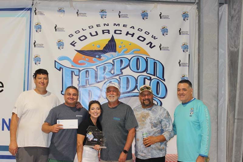 A group of people are posing for a picture in front of a tarpon rodeo banner.