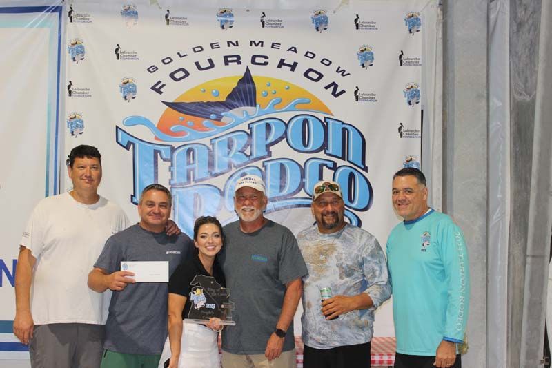 A group of people are posing for a picture in front of a tarpon rodeo banner.