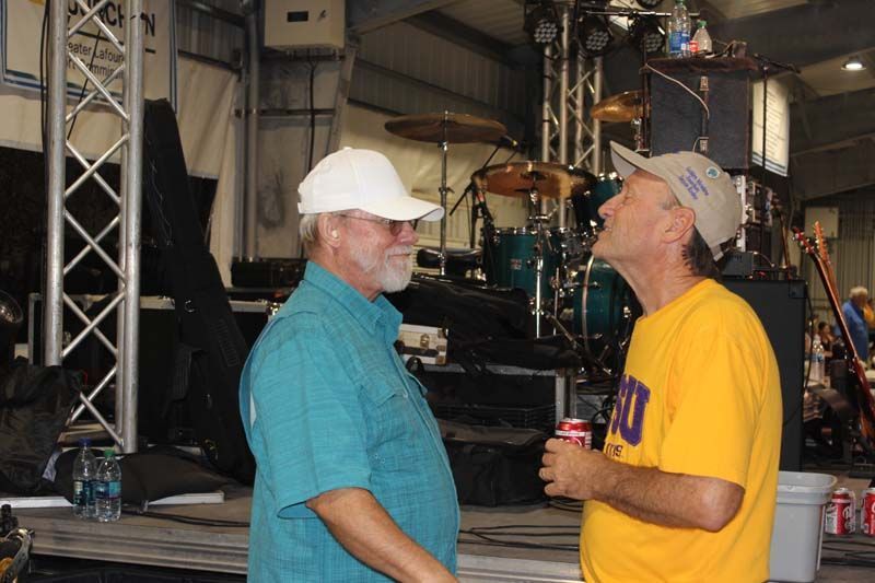 Two men are standing next to each other and talking in front of a drum set.