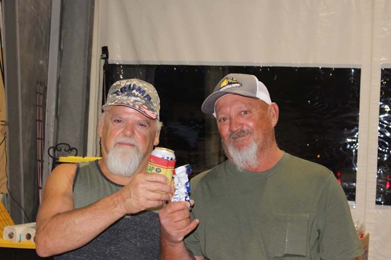 Two men are standing next to each other holding cans of soda.