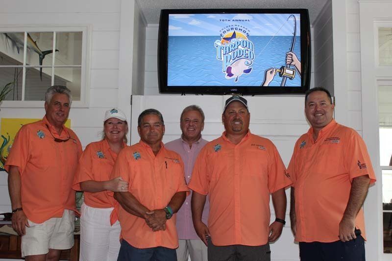 A group of men are posing for a picture in front of a television that says fishing rival