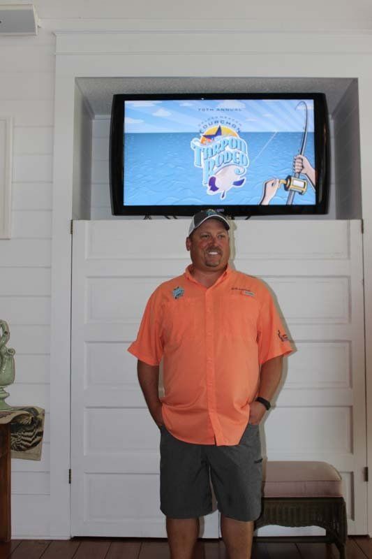 A man in an orange shirt is standing in front of a flat screen tv.