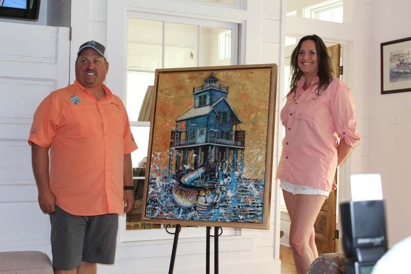 A man and a woman are standing next to a painting of a lighthouse.
