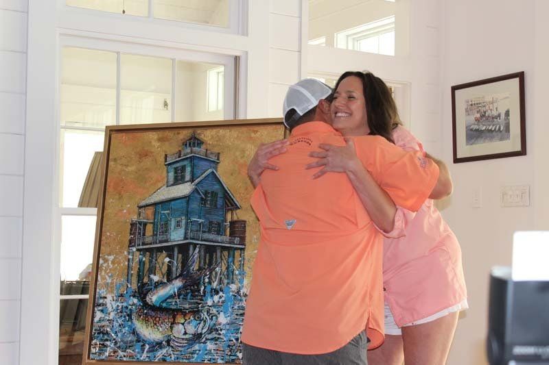 A woman is hugging a man in front of a painting of a lighthouse.
