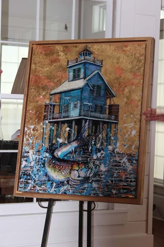 A painting of a house on stilts in the water on an easel.