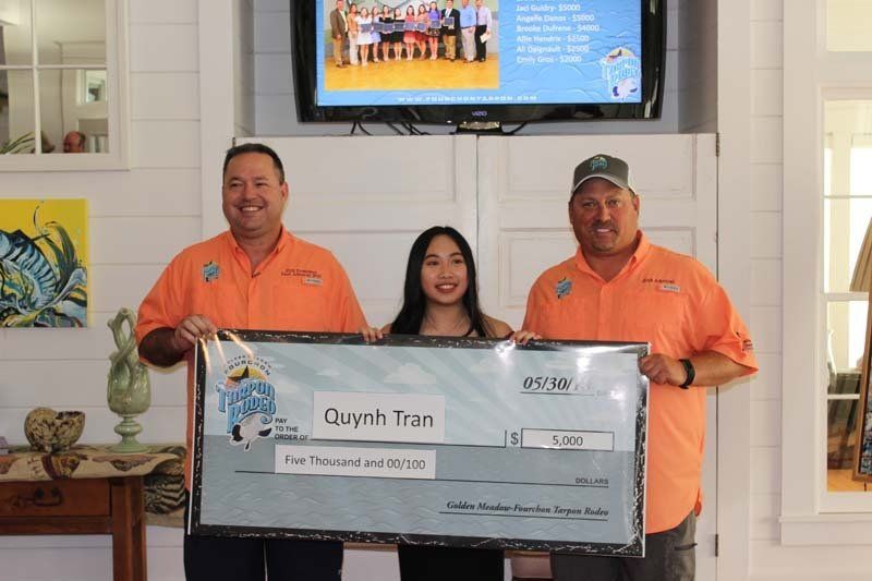 Two men and a woman are holding a large check in front of a television.