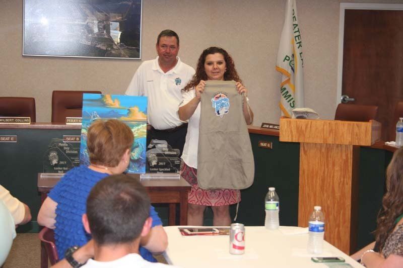 A woman is holding a shirt in front of a group of people