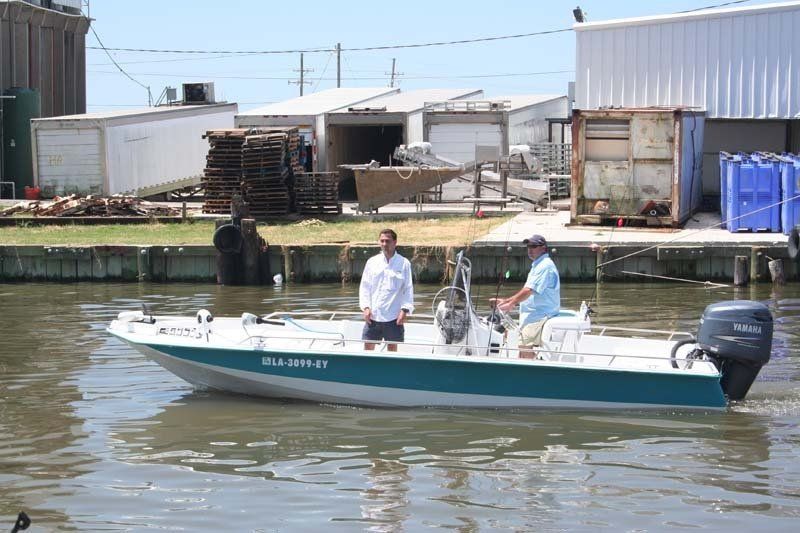 Two men are standing on a boat in the water near a dock.