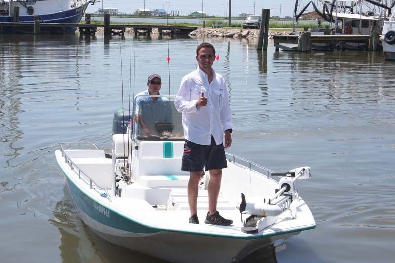 A man is standing on a boat in the water giving a thumbs up.