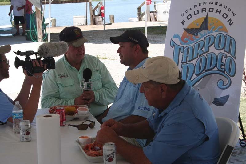 A group of men are sitting at a table in front of a tarpon rodeo banner