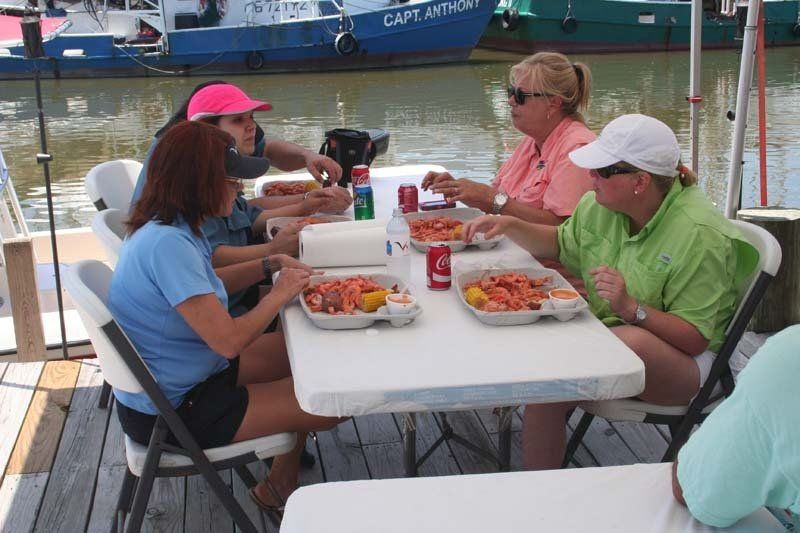 A group of people sitting around a table with a boat in the background that says captain anthony