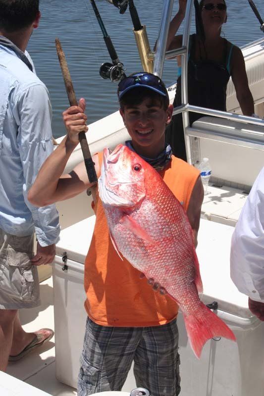A young boy is holding a large red fish on a boat