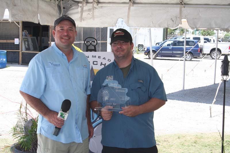 A man holding a microphone stands next to another man holding a trophy