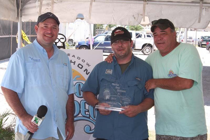 Three men are posing for a picture under a tent and one of them is holding a trophy