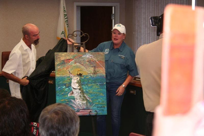 A man and a woman are holding a painting in front of a crowd.