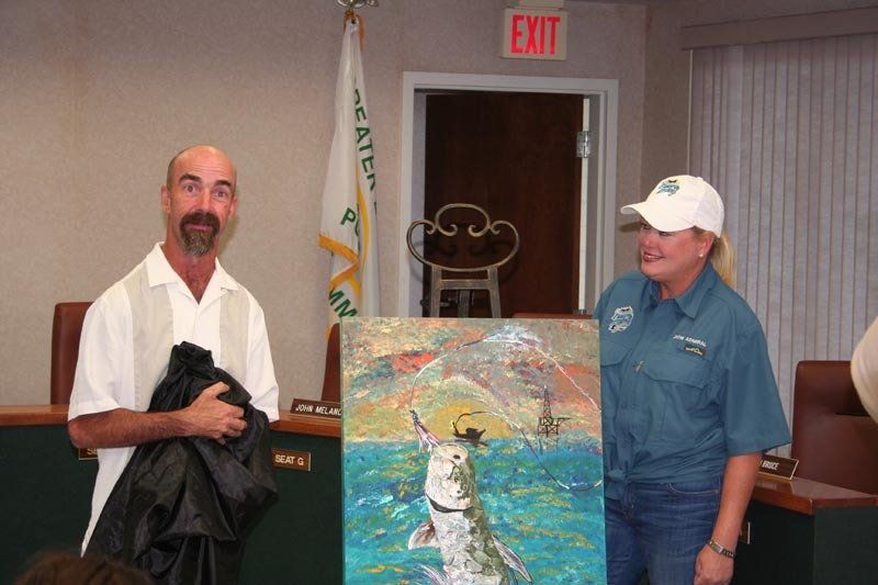 A man and a woman are holding a painting of a fish in front of an exit sign
