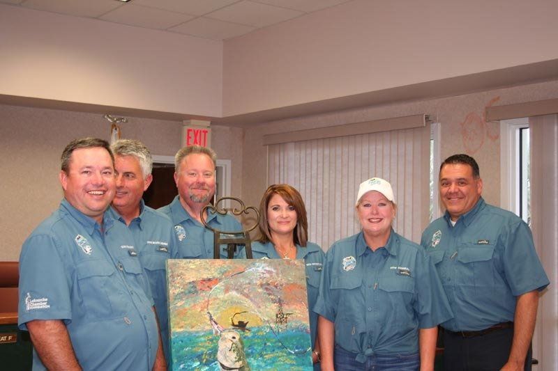 A group of people standing next to each other holding a painting.