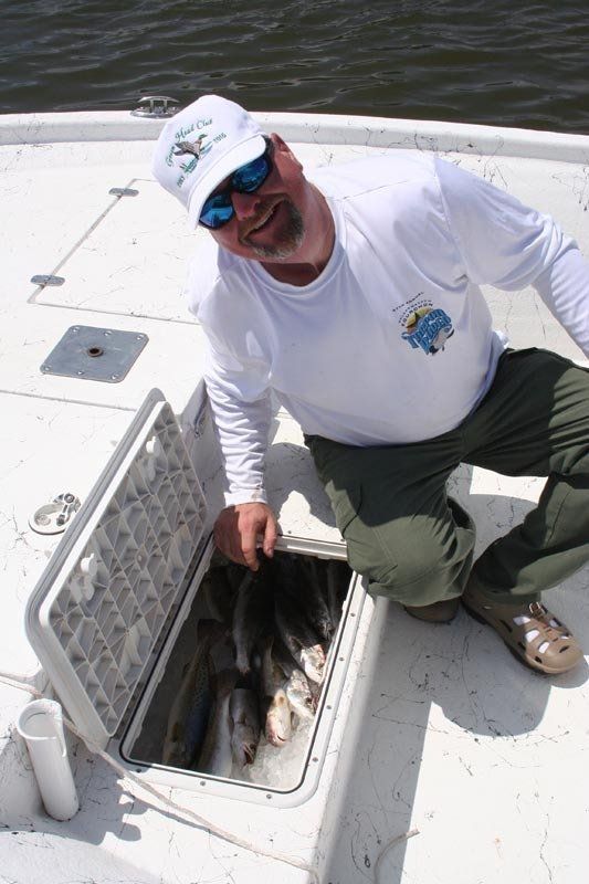 A man is kneeling on a boat with a cooler full of fish.