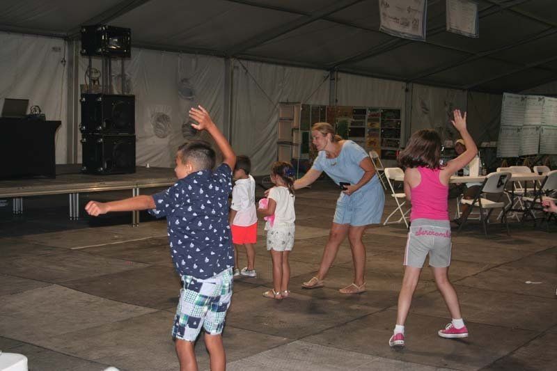 A group of children are dancing with a woman in a tent.