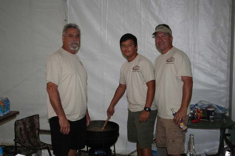 Three men are standing next to each other in front of a large pot.