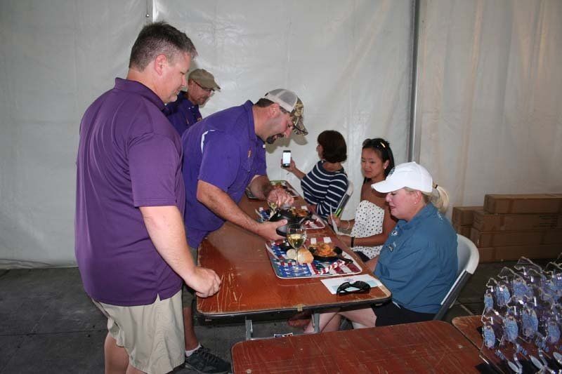 A group of men in purple shirts are standing around a table